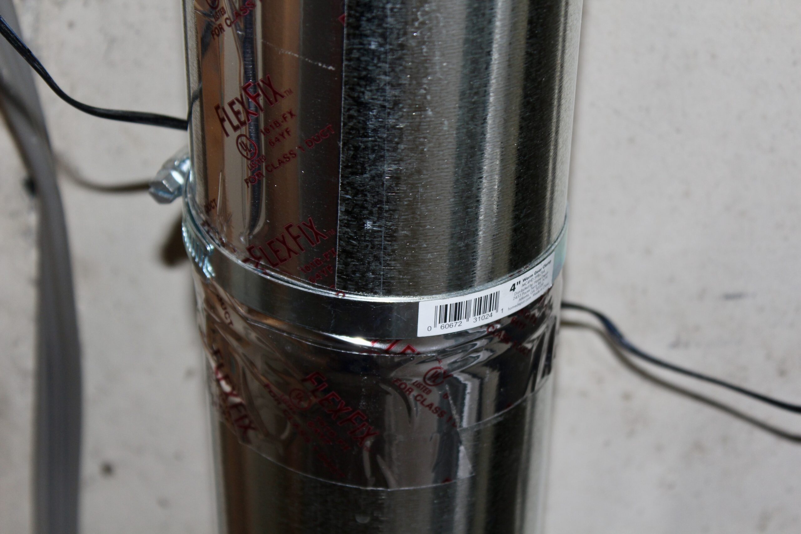 Vertical run of rigid aluminum dryer duct with a joint sealed in aluminum foil tape and secured with a metal clamp