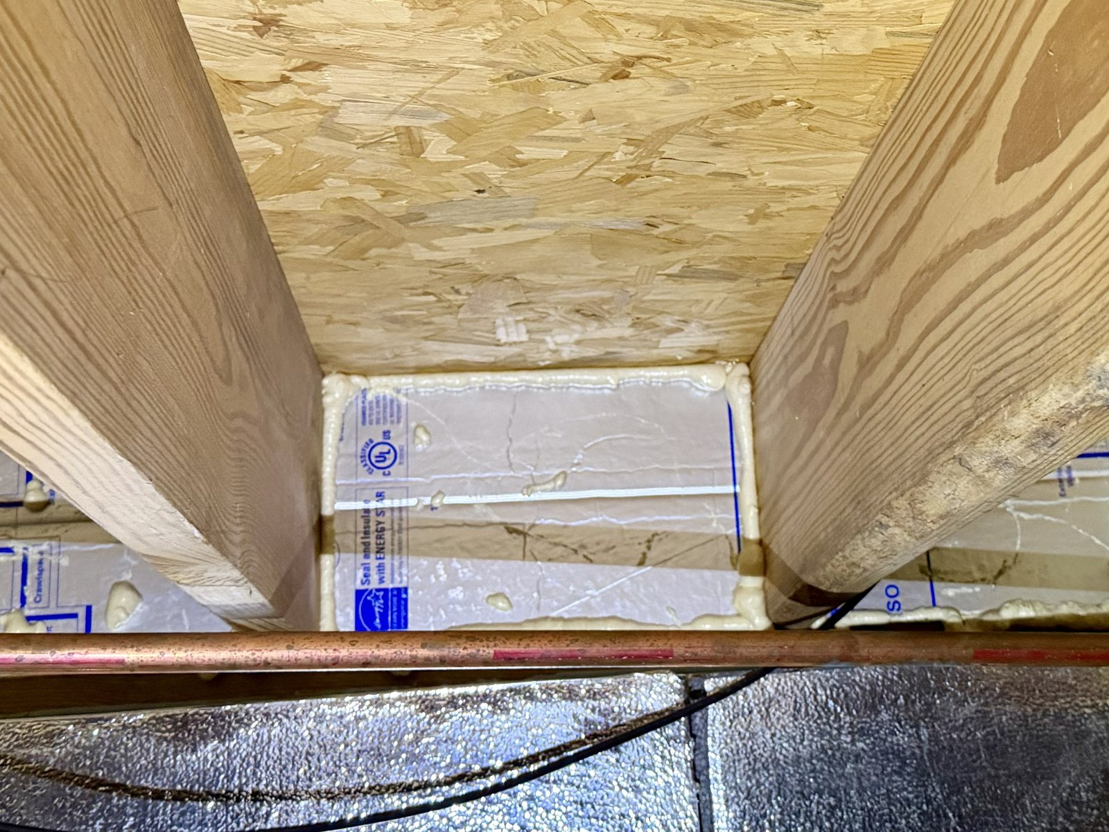 Two insulated joist bays showing foam board fitted against the rim joist, with a copper pipe running in the foreground