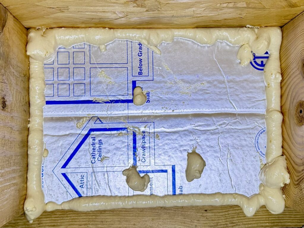 Close-up of foil-faced foam board fitted in a single joist bay, with spray foam sealing the edges